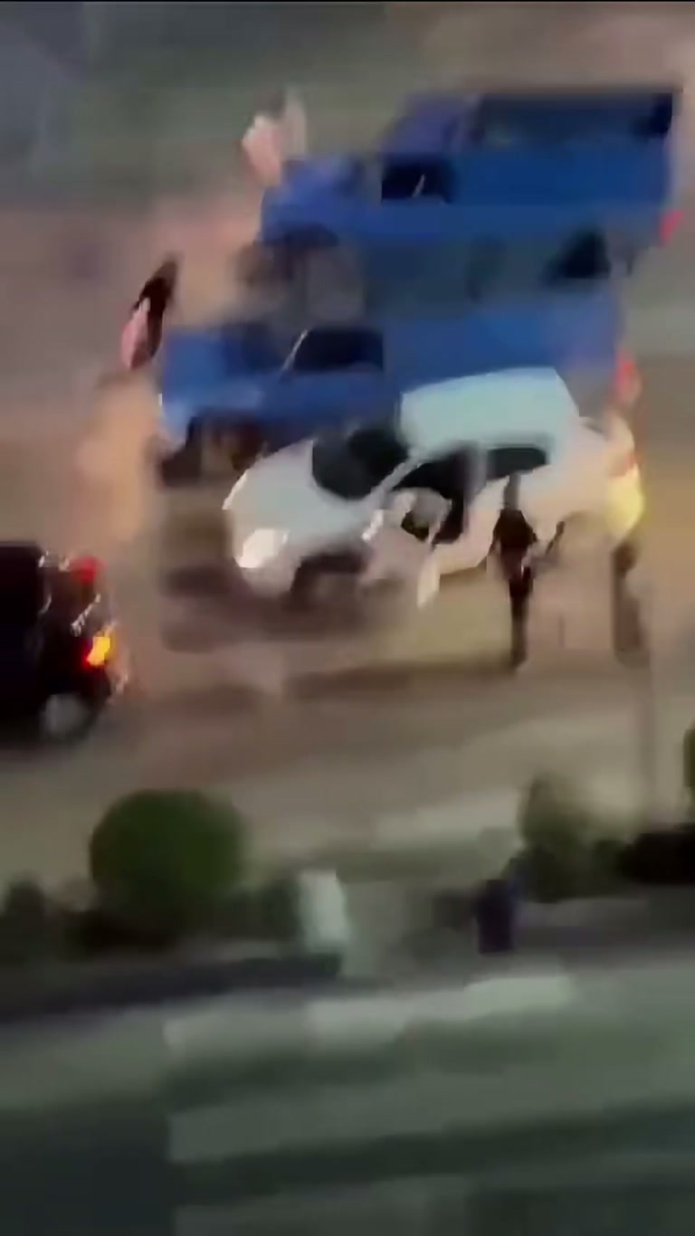 Night Street Chaos: White Car, Blue Truck, and a Crowd