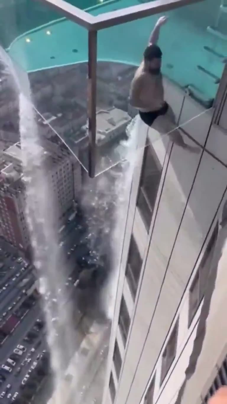 Man Clings to Glass Sky Pool Edge as Water Pours Down Below