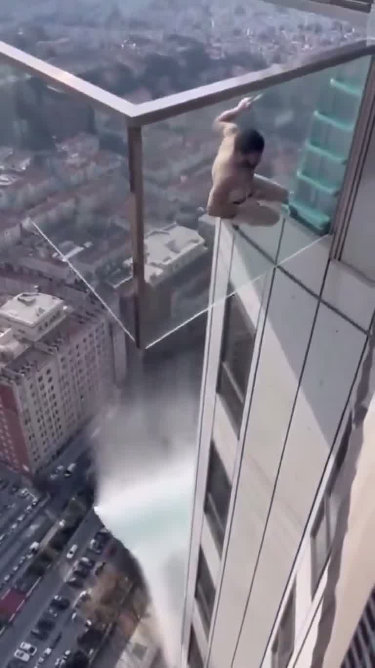 Man Clings to Glass Sky Pool Edge as Water Pours Down Below