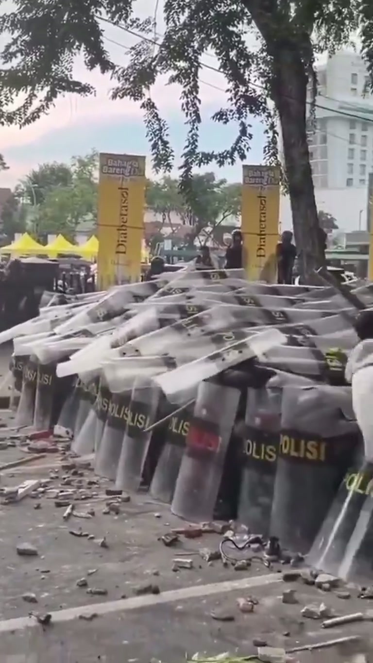 Pink Shirt and Police Shields: Chaos on a Debris-Strewn Street