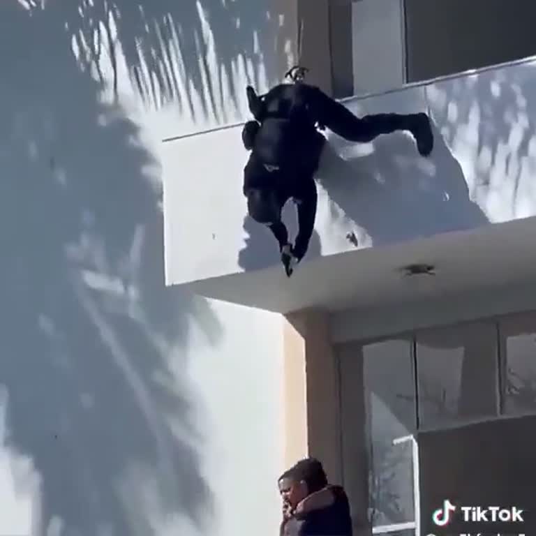 A Figure in Black Ropes Down a White Facade as Cameras Roll