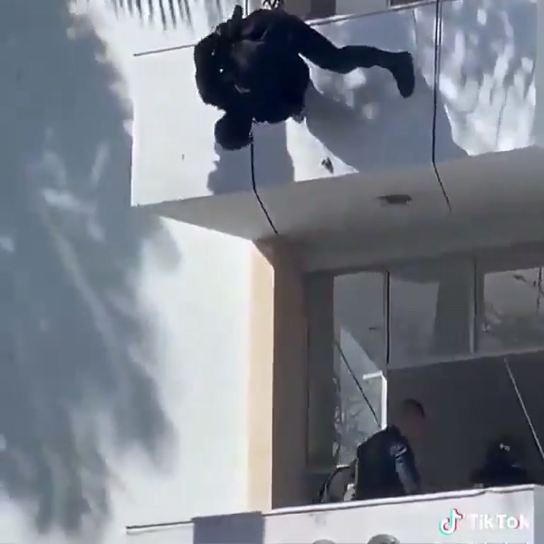 A Figure in Black Ropes Down a White Facade as Cameras Roll